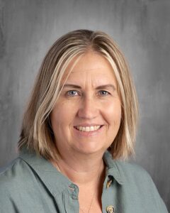 Professional portrait of a woman with shoulder-length blonde hair, smiling, wearing a green button-up shirt, against a neutral gray background. Ideal for showcasing personal branding or educational profiles.