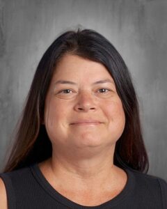 Professional headshot of a woman with long dark hair, wearing a sleeveless black top, smiling against a neutral gray background.
