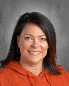 Smiling woman with shoulder-length dark hair wearing an orange hoodie, set against a gray background.