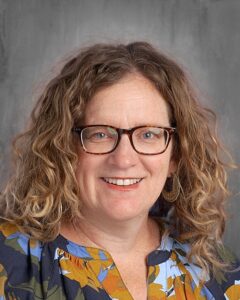 Smiling woman with curly hair wearing glasses and a floral blouse, featuring a neutral background, suitable for professional profiles or educational contexts.